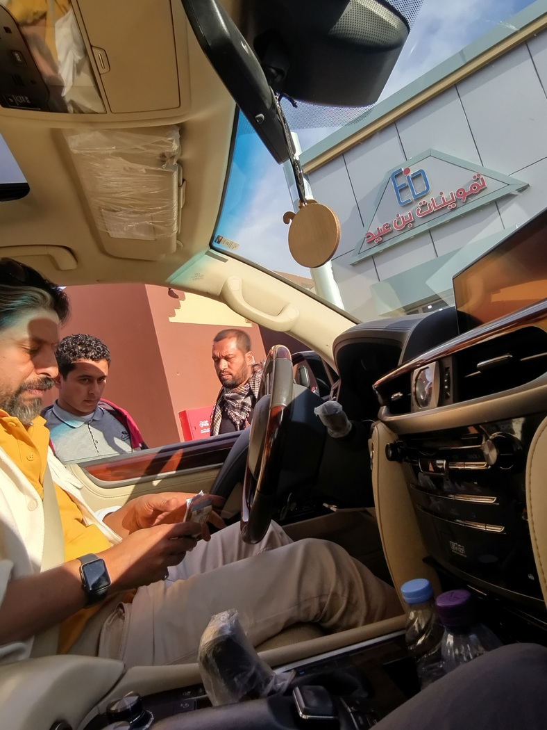 Ahmed zählt auf dem Fahrersitz Geld, 2 Männer schauen zum Fenster rein